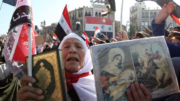 A Syrian woman holds up a copy of the Muslim holy Quran next to a Christian icons, during a demonstration in the capital Damascus on November 28, 2011. (AFP/File)