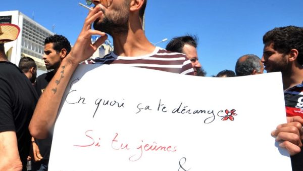 A Tunisian protester smokes a cigarette and holds a placard reading in French "Why is it bothering you? If you fast and I eat?" during a demonstration for the right to eat and smoke in public during the Muslim dawn-to-dusk fasting month of Ramadan, on June 11, 2017, in Tunis. (Sofienne Hamdaoui/AFP)