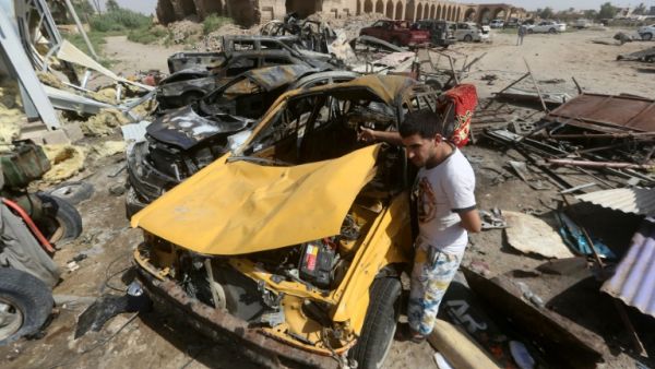 An Iraqi man stands next to the wreckage of cars in the aftermath of a massive suicide car bomb attack. (AFP)