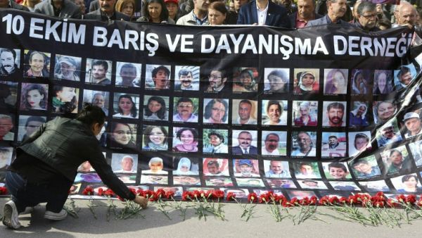 A wonam lays red carnations as people hold a banner with pictures of victims of October 10 bombings during a memorial ceremony in Ankara on April 10, 2016. (AFP/Adem Altan)