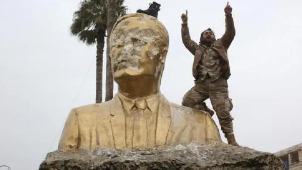 A militant from the Army of Conquest alliance destroys a statue of Bashar al-Assad in Syria's Idlib Province. (Al Bawaba/File)