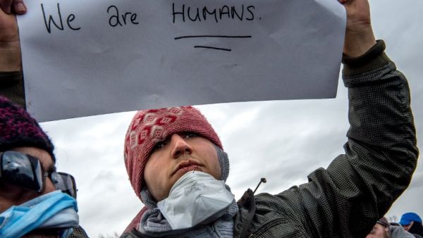 An Iranian migrant with sewn lips holds a placard reading "we are humans" as he protests during the demolition of the southern part of the so-called "Jungle" migrant camp, on March 2, 2016, in Calais. (AFP/Philippe Huguen)