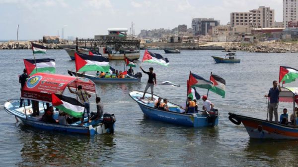 Palestinians hold their national flag as they ride boats during a rally to show support for activists aboard the flotilla (AFP Photo/Mahmud Hams)
