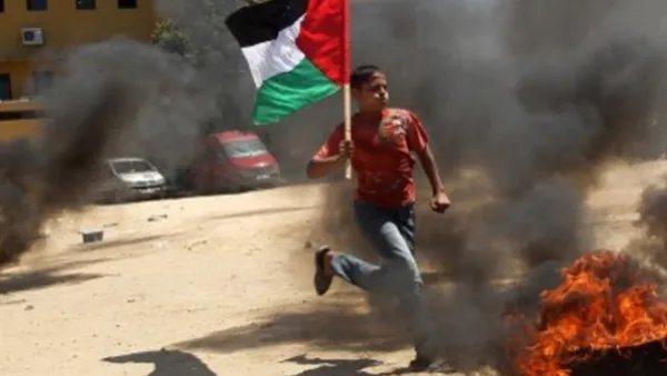 طفل فلسطيني يرفع العلم الفلسطيني ويقفز عن اطار مشتعل اثناء تدريب في غزة/أ.ف.ب