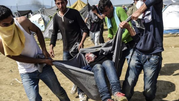 Migrants and refugees carry a man injured during clashes with Macedonian soldiers near their makeshift camp in the northern Greek border village of Idomeni, on April 10, 2016. (AFP/Bulent Kilic)