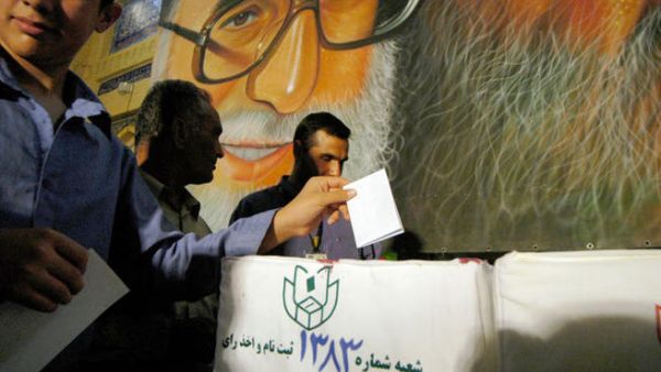 Iranian men cast their ballots beneath a poster of Ayatollah Ali Khamenei during the Iranian presidential election. (Image credit: Getty)