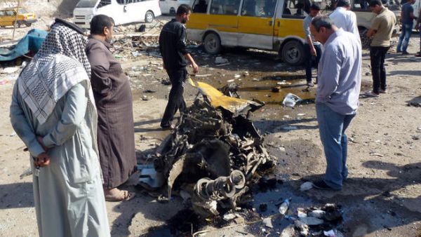 Iraqis look at the remains of a vehicle following an explosion at a small bus station . (Image credit: AFP)