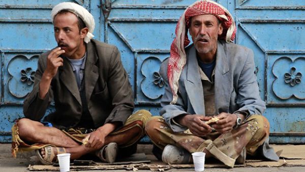 Unemployed Yemeni manual laborers eat as they wait for work offers on a sidewalk in Sanaa. (AFP/File)
