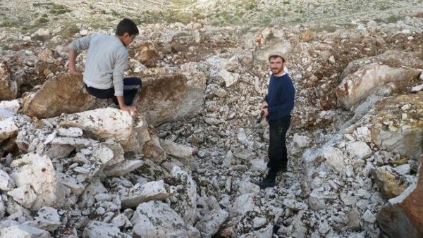 Syrian men stand inside a crater where they said a Scud missile landed near the military base of Sheikh Suleiman on the outskirts of the northwestern town of Darret Ezza on Friday. (AFP PHOTO / HERVE BAR)