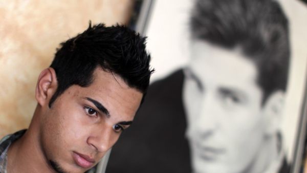 A Palestinian youth poses for a picture next to a poster after getting a stylish haircut at barber's shop in Gaza City. (AFP PHOTO/MAHMUD HAMS)