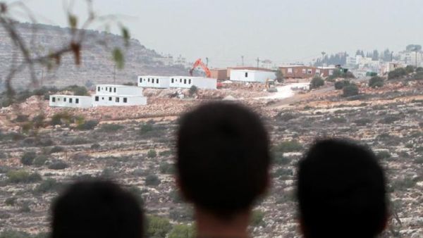 Palestinian children look at bungalows built by Israeli settlers on seized land, near the West Bank city of Birzeit on December 3, 2013. [AFP]