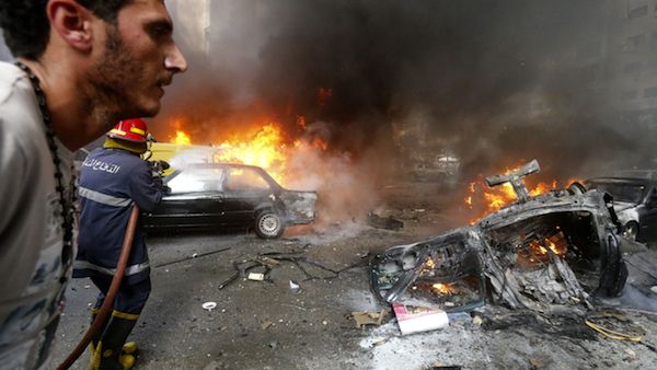 A man walks past as a firefighter extinguishing fire at the site of an explosion in Beirut's southern suburb Bir al-Abed (Source: AFP/STR)