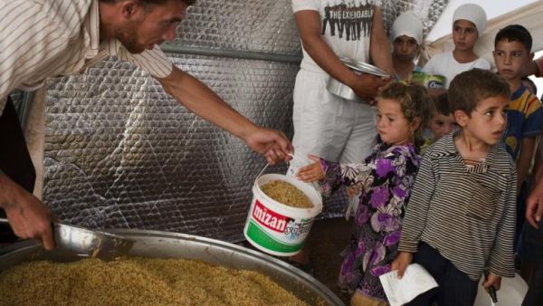 A volunteer shares out food to the people in the Bab al-Salam refugee camp for displaced Syrians near the border with Turkey on 2 July 2013. (AFP/File)