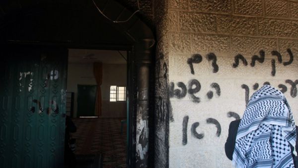 A Palestinian man looks at graffiti scrawled at the entrance to a mosque that reads in Hebrew, "Arabs out" and "Revenge for blood spilled in Qusra" in the West Bank village of Deir Istiya which lies next to the Israeli settlement of Ariel on Tuesday.
