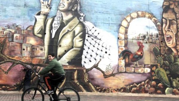 A Palestinian boy cycles past a mural painted by university students depicting the late Palestinian leader Yasser Arafat in the West Bank city of Nablus on November 9, 2013. (AFP)