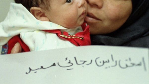 Jordanian infant Yitzhak Rabin and his mother Miriam hold a paper with his name at their home in Jordan, in March 1996, shortly after the government permitted the boy to carry the name of the slain Israeli prime minister. [Al-Arabiya]