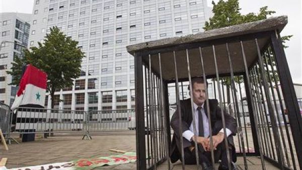 رجل يرتدي قناعا للرئيس السوري يجلس في قفص اتهام اثناء احتجاج ضد الحكومة السورية امام المحكمة الجنائية الدولية في لاهاي
