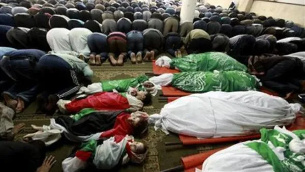 فلسطينيون يصلون بجوار حثامين افراد من عائلة الدلو قبل تشييع جنازتهم في غزة
