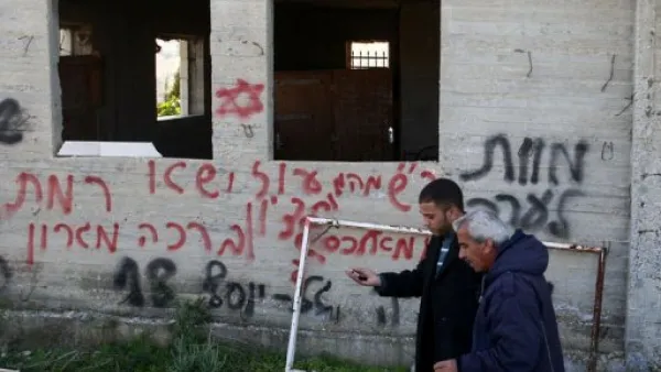 فلسطينيان يمران امام جدار عليه عبارات بالعبرية كتبها مستوطنون بالقرب من رام الله بالضفة الغربية
