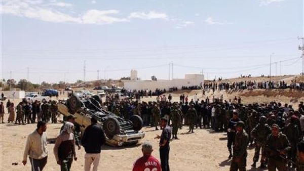 جنود من الجيش التونسي وسكان ولاجئين ليبيين بالقرب من سيارة مقلوبة تابعة للقوات القذافي بالقرب من الذهيبة 
