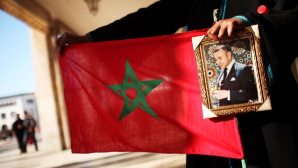 A woman holds a Moroccan flag and a portrait of King Mohammed VI at a protest in 2011. (Source: Spencer Platt / Getty)