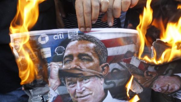 A protester holds a poster burning on which is depicted former US president George W. Bush taking off a mask of current President Barack Obama during a demonstration of in Beirut. (AFP)
 A protester holds a poster burning on which is depicted former US president George W. Bush taking off a mask of current President Barack Obama during a demonstration of in Beirut. (AFP)