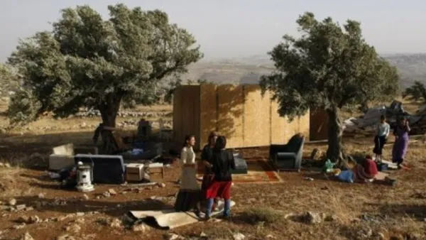 مستوطنون يقفون الى جانب كوخ من الخشب اعيد بناؤه في مستوطنة ميغرون العشوائية في الضفة الغربية 
