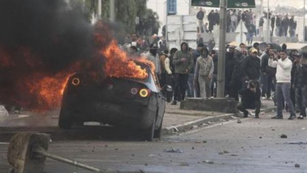 محتجون يشاهدون سيارة تحترق خلال اشتباكات مع الشرطة قرب المقبرة الذي دفن بها المعارض شكري بلعيد بتونس العاصمة يوم الجمعة
