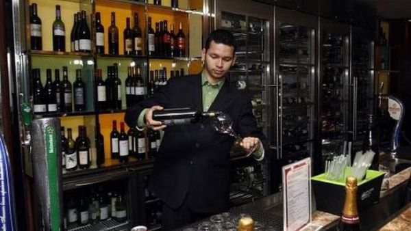 A bartender pours wine into a wine glass.