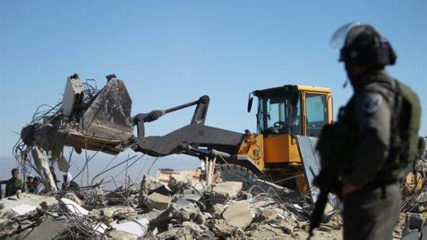 An Israeli soldier stands as a bulldozer pulls down the house of a Palestinian family near the West Bank town of Hebron. (AFP/Hazem Bader)
