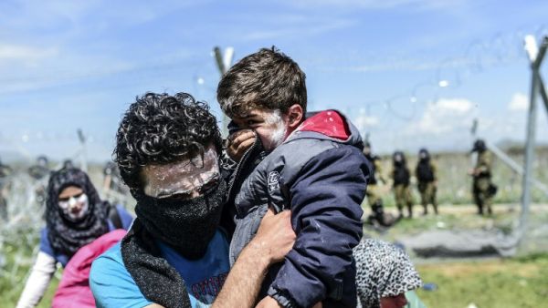 A family with toothpaste smeared over their faces as a protection against teargas, moves to safety as refugees and migrants clash with Macedonian police during a protest to reopen the border near their makeshift camp in the northern Greek border village of Idomeni, on April 10, 2016. (AFP/Bulent Kilic)