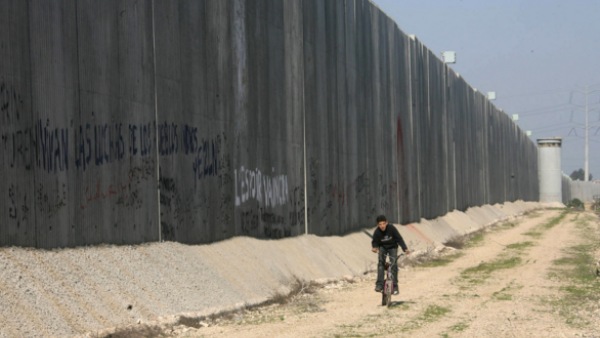 A Palestinian boy rides his bicycle past a separation wall in the West Bank. (AFP/File)