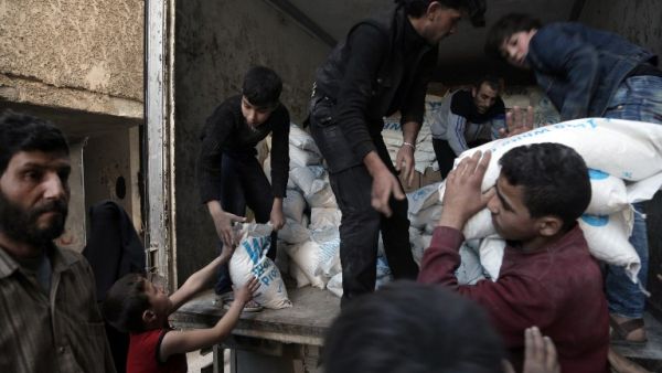 Syrian children carry sacks of wheat, provided by the World Food Programme (WFP), in Kafr Batna, in the rebel-held Eastern Ghouta area, outside Damascus on March 1, 2016. (AFP/Amer Almohibany)