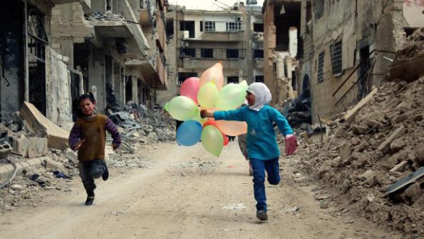 Syrian children run with balloons past heavily damaged buildings in the neighbourhood of Jobar, on the eastern outskirts of the Syrian capital Damascu. (AFP/File)
