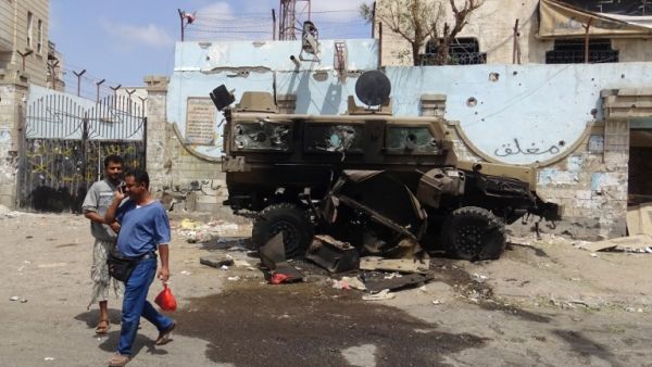 Yemeni men walk on March 13, 2016 past a charred car damaged during clashes between suspected al-Qaeda militants and policemen a day earlier, in the Mansoura residential district of the port city of Aden. (AFP/Saleh al-Obeidi)