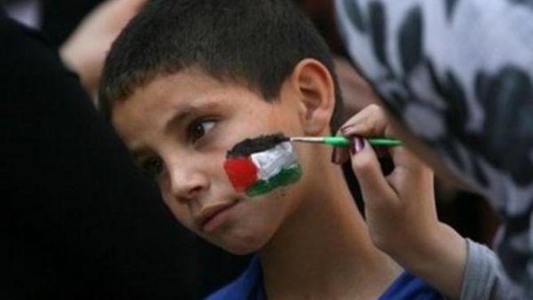 متظاهرة يمنية ترسم علم فلسطين على وجه احد الأطفال المشاركين