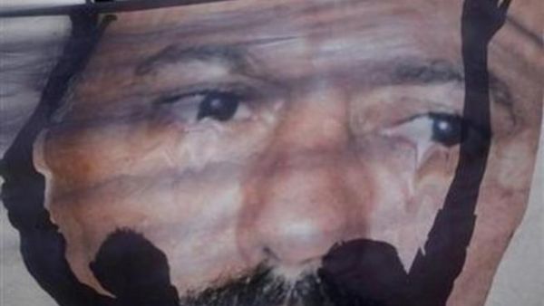 متظاهرون يقومون بفرد ملصق كبير لصالح استعدادا لتمزيقه خارج جامعة صنعاء