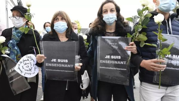 أشخاص يحملون لافتات كتب عليها "أنا مدرّس -- حرية التعبير" أمام مدرسة في كونفلان سانت اونورين.