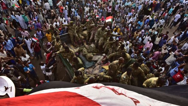 Sudanese demonstrators surround soldiers as they gather near the military headquarters in the capital Khartoum  (AFP)