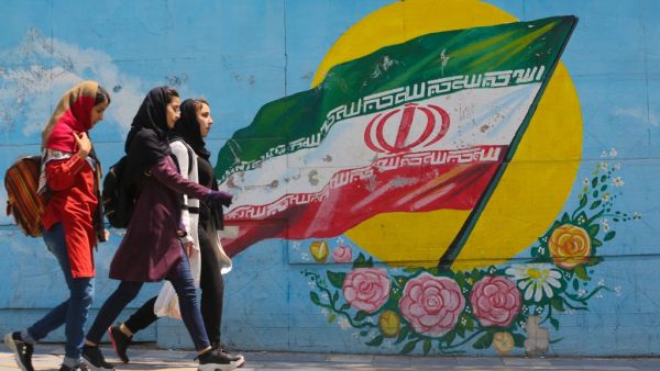 Young girls walk in front of a mural showing the Iranian national flag (AFP)