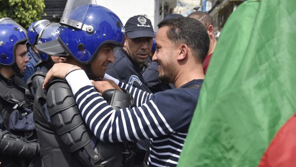 An Algerian man, embraces a member of the security forces during an anti government demonstration in the capital Algiers on April 23, 2019.  RYAD KRAMDI / AFP