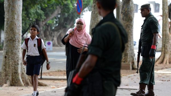 Sri Lankan security personnel stand guard as a school student (L) returns to classes as schools re-open across the country after the Easter attacks in Colombo (AFP)