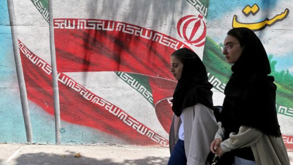 Iranian women walk past a mural painted with the Iranian flag in Tehran (AFP)