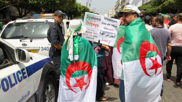 Algerian protesters, drapped in national flags, walk past a police officer during a weekly demonstration coinciding with the Algerian independence day in the capital Algiers  (AFP)