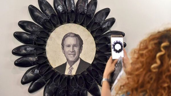 A visitor takes a picture of George W. Bush surrounded by black shoes during the opening of the Beirut Art Fair  (Twitter)