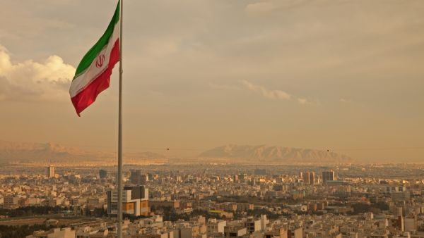 Iran flag waving in the wind above skyline of Tehran (Shutterstock)	