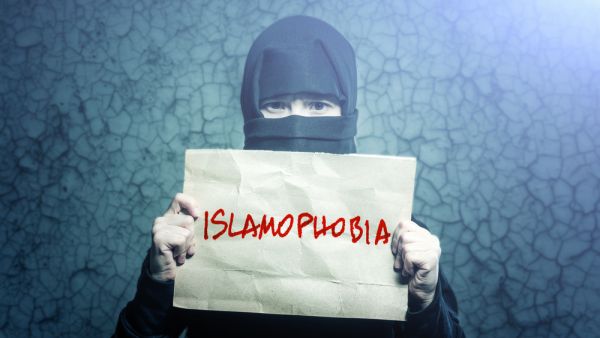 Muslim girl in black hijab holding a poster with an inscription ISLAMOPHOBIA (Shutterstock)