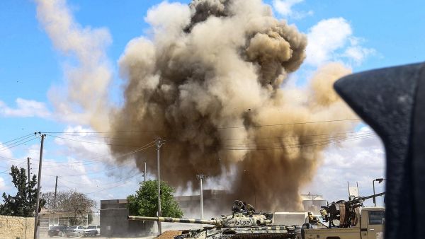 This picture taken on April 12, 2019 shows a smoke plume rising from an air strike behind a tank and technicals belonging to forces loyal to Libya's Government of National Accord. (Mahmud TURKIA / AFP)