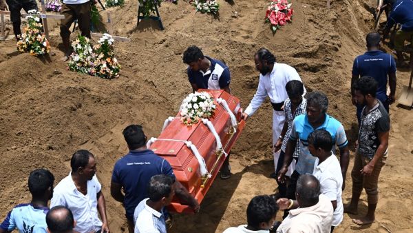 Relatives (R) watch as workers place the coffin of a bomb blast victim during a burial ceremony at a cemetery in Negombo on April 23, 2019. (AFP/ File)