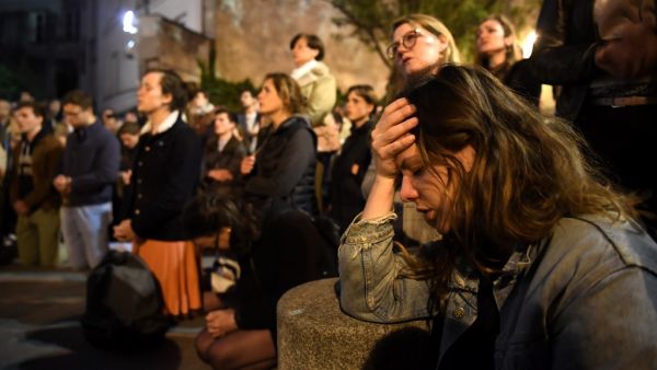 People kneel on the pavement as they pray outside watching flames engulf Notre-Dame Cathedral in Paris on April 15, 2019. A colossal fire swept through the famed Notre-Dame Cathedral in central Paris on April 15, 2019. (AFP)